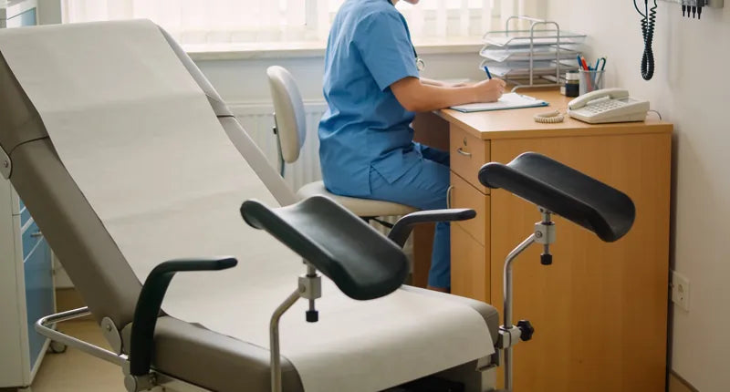 Doctor's office with examination table and chair, and a doctor at a desk with medical records.